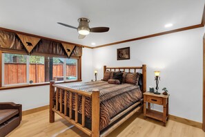 A bedroom with a wooden bed, a nightstand, a ceiling fan, and a window with a view of a wooden fence. - Private Pool & Hot Tub! Luxe South Lake Tahoe Gem (South Lake Tahoe)