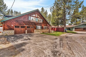 A rustic cabin with a stone foundation, wooden garage doors, and a large window overlooking a grassy yard. - Private Pool & Hot Tub! Luxe South Lake Tahoe Gem (South Lake Tahoe)