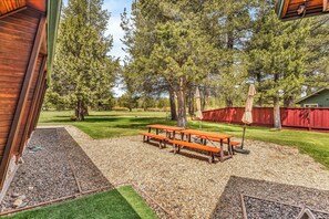 Un patio trasero con una mesa de picnic, una cerca roja y un césped verde.