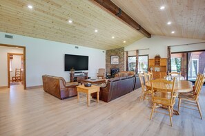 Ein geräumiges Wohnzimmer mit Holzboden, einem Wand-Fernseher, einem Kamin und einem Essbereich mit Holzsesseln und einem Tisch.