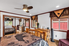Ein Schlafzimmer mit einem Bett, einem Schreibtisch, einem Stuhl, einem Deckenventilator und einem Fenster mit Blick auf ein rotes Gebäude.