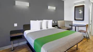 Quarto de hotel com cama, mesa de cabeceira, cadeira e pequena escrivaninha com cadeira.