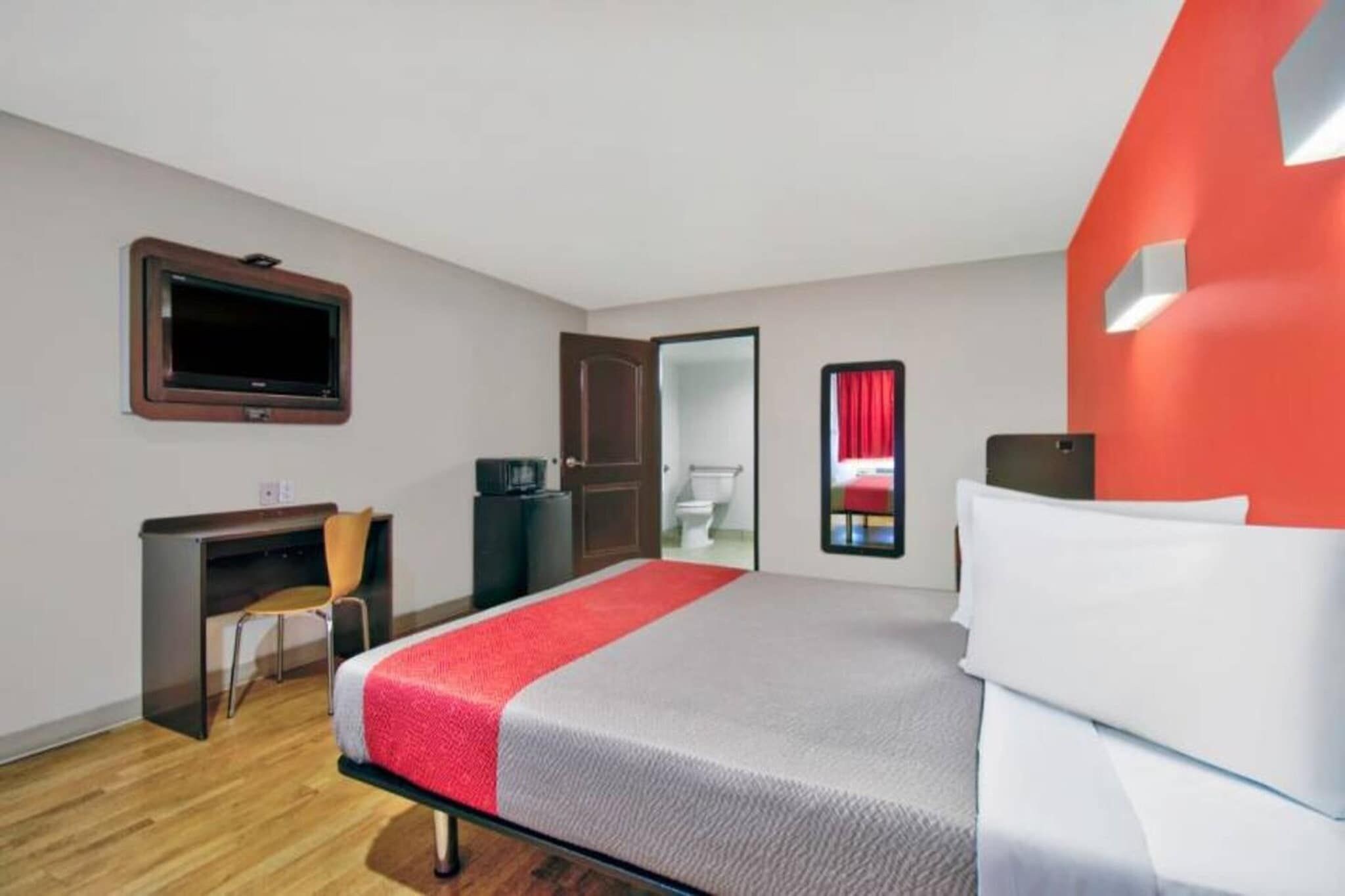 A hotel room with a bed, a desk, a chair, a television, and a door leading to a bathroom.