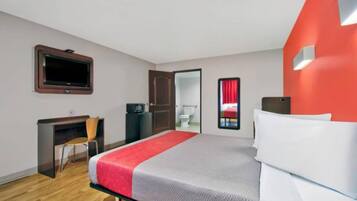 A hotel room with a bed, a desk, a chair, a television, and a door leading to a bathroom.