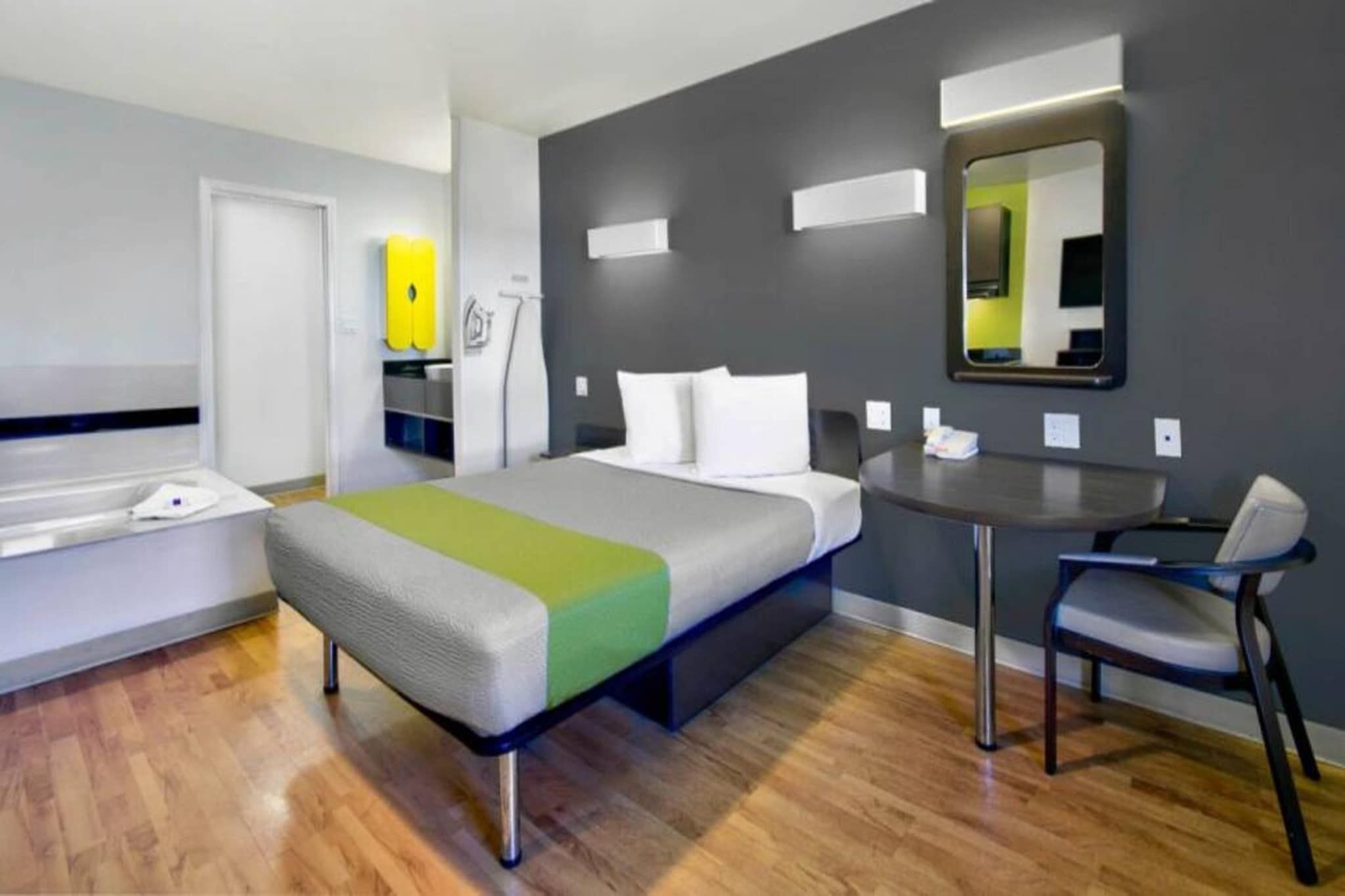 Una habitación de hotel con cama, escritorio, silla, espejo y baño.