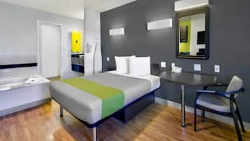 Una habitación de hotel con cama, escritorio, silla, espejo y baño.
