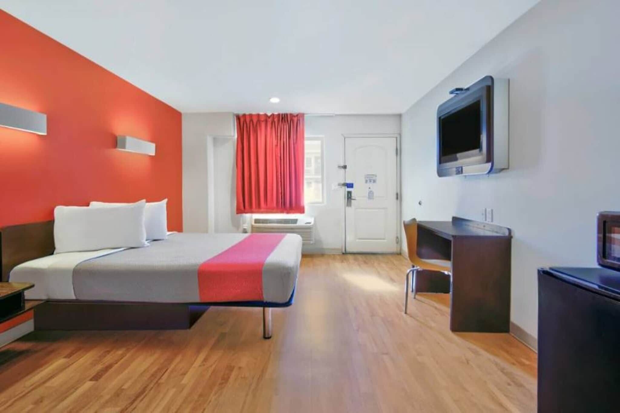 Una habitación de hotel con cama, escritorio, silla, televisor y puerta.