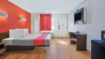 A hotel room with a bed, a desk, a chair, a TV, and a door.