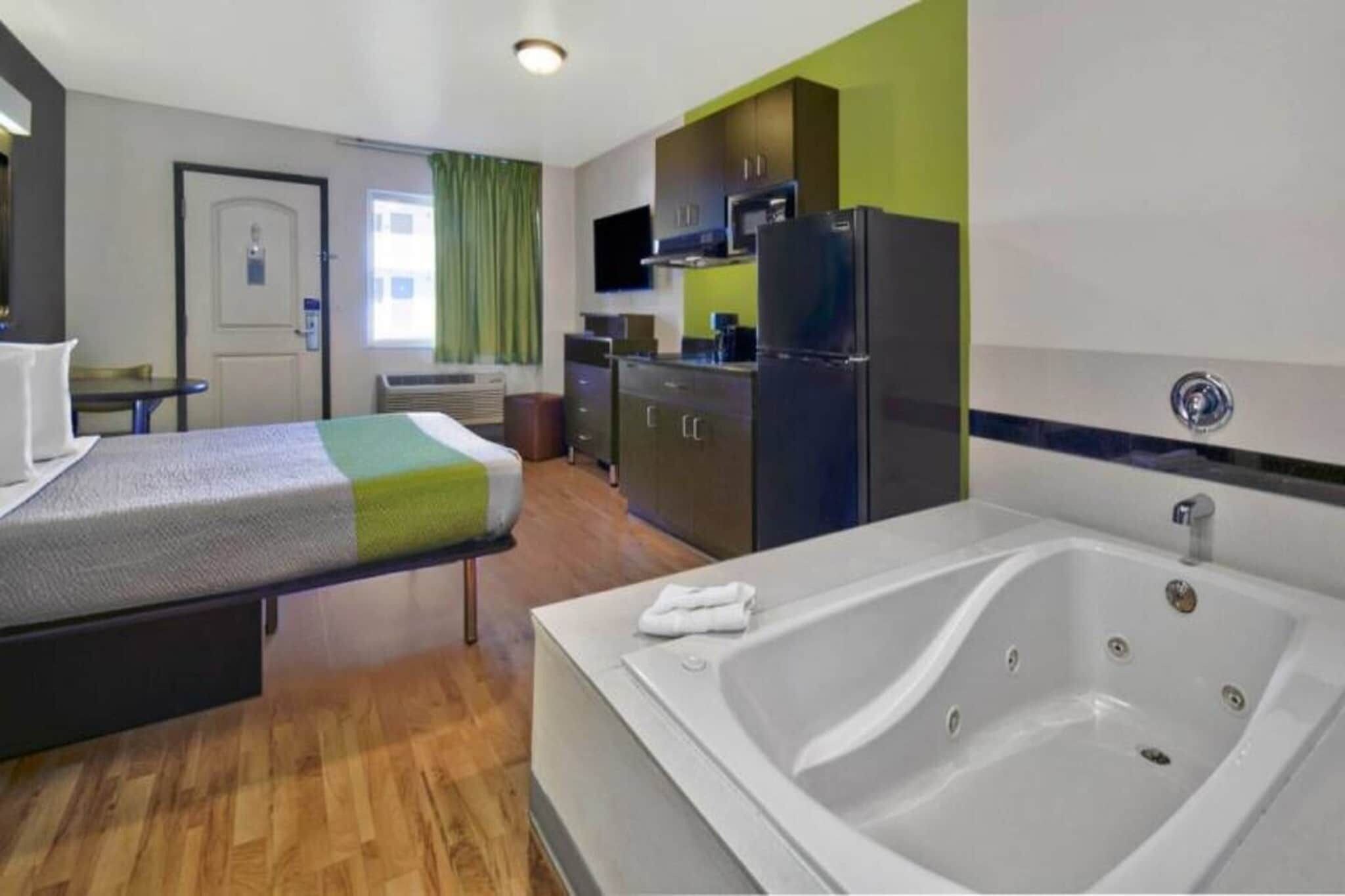 Habitación de hotel con cama, baño con bañera, kitchenette y televisor.