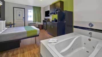 A hotel room with a bed, a bathroom with a bathtub, a kitchenette, and a television.