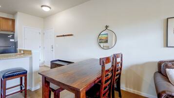 A dining area with a wooden table and chairs, a kitchen with a refrigerator, and a wall-mounted mirror.