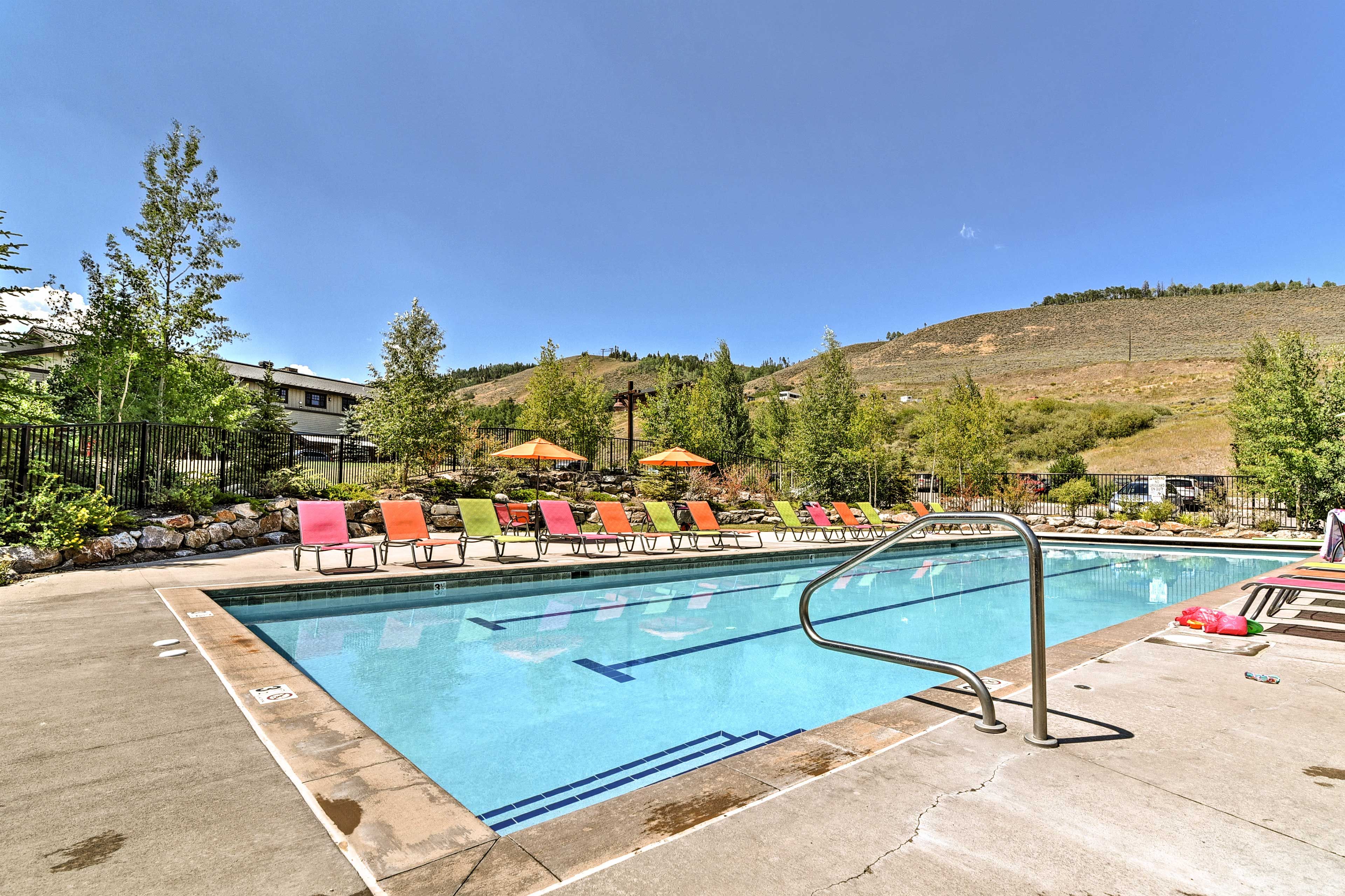 A swimming pool with a metal ladder, surrounded by lounge chairs with colorful towels.