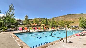 A swimming pool with a metal ladder, surrounded by lounge chairs with colorful towels.