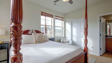 A four-poster bed with a wooden finish, a nightstand with a lamp, a chair, and a window with blinds.