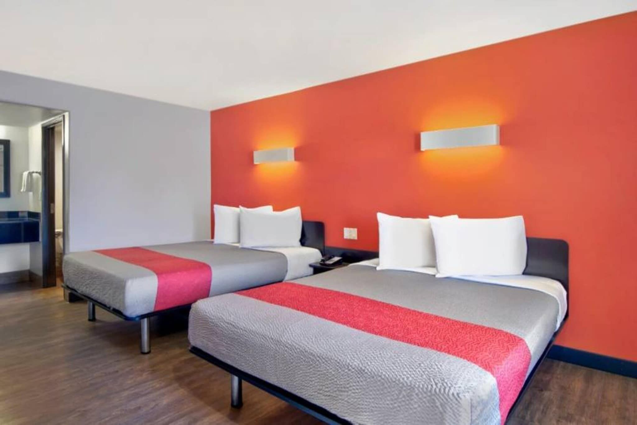 Ein Hotelzimmer mit zwei Betten, jeweils mit einer roten und grauen Tagesdecke, weißen Kissen und einem Holzboden.