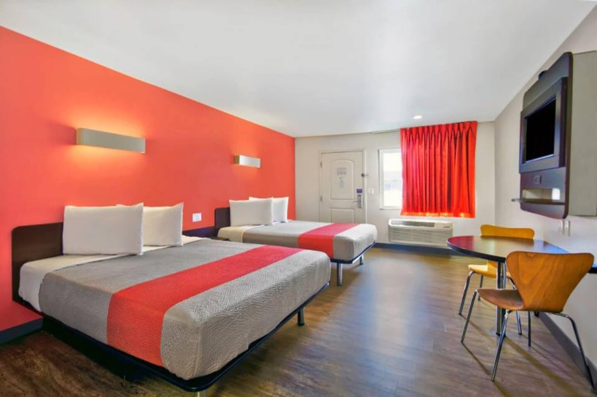 A hotel room with two beds, a desk, and a TV.