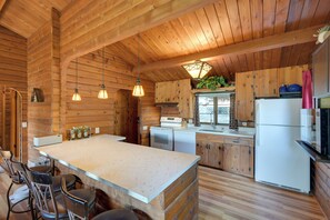 Interior de una cabaña de madera con zona de cocina, barra y una isla grande.