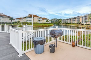 Ein Deck am Wasser mit Grill, Mülleimer und Blick auf Wohnhäuser am See.