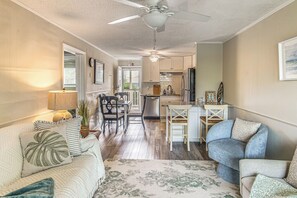 Ein geräumiges Wohnzimmer mit einer Couch, einem Essbereich mit Stühlen, einer Küche mit Kühlschrank und einem Deckenventilator.