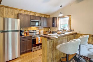 Una cocina con armarios de madera, electrodomésticos de acero inoxidable y una barra con dos taburetes.