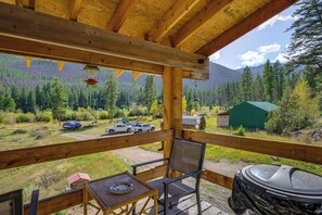 Une terrasse en bois offrant une vue sur une chaîne de montagnes boisées, une table de pique-nique couverte et un barbecue.