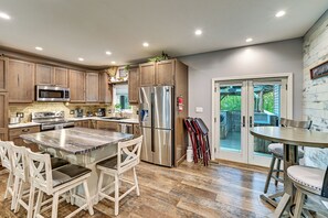 A modern kitchen with wooden cabinets, stainless steel appliances, a marble island, and a view to a patio area. - Hot Tub, Game Room & Steps to Pond! Elkhart Escape (Elkhart)