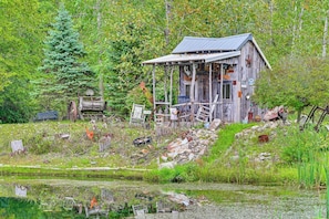 A rustic cabin with a porch, surrounded by a pond and dense forest. - Hot Tub, Game Room & Steps to Pond! Elkhart Escape (Elkhart)