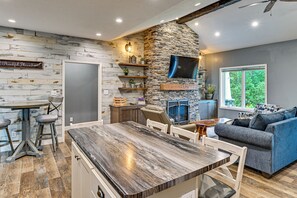 A modern kitchen with a stone accent wall, a dining area with a wooden table, and a living room with a blue sofa. - Hot Tub, Game Room & Steps to Pond! Elkhart Escape (Elkhart)