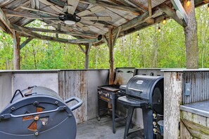 An outdoor barbecue area with a grill and a portable stove, surrounded by a rustic wooden structure. - Hot Tub, Game Room & Steps to Pond! Elkhart Escape (Elkhart)