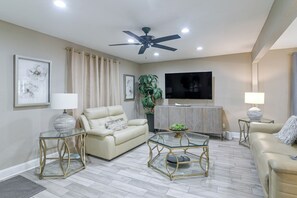 A modern living room with a ceiling fan, a flat-screen TV, and a sofa. - 3 Mi to Hobby Airport! Retreat w/ Poolside Oasis (Houston)