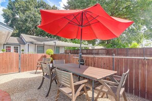 An outdoor patio with a wooden table and chairs, a red umbrella, and a wooden fence. - 3 Mi to Hobby Airport! Retreat w/ Poolside Oasis (Houston)