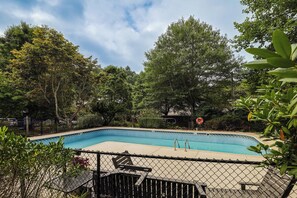 Ein Pool, umgeben von einem Zaun, mit Bäumen und blauem Himmel im Hintergrund.