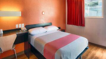 Una habitación de hotel con una cama, una mesita de noche con teléfono, una silla y una ventana con cortinas.