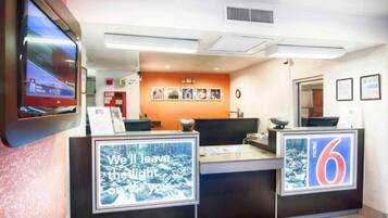 Una mesa de recepción con una pantalla digital mostrando una imagen panorámica, un cartel con el número 6 y un cuadro con una imagen de un bosque.