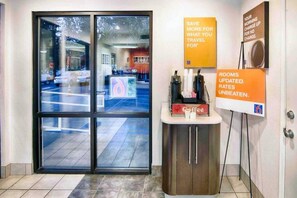 A hotel reception area with a glass door entrance, a coffee station, and informational signs about room rates and amenities. - 1 Full Bed | ADA/Tub (Mammoth Lakes)
