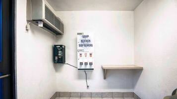 Un baño pequeño con un calentador en la pared, dispensador de jabón y un estante.
