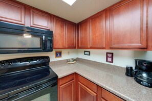A kitchen with wooden cabinets, a black microwave, a stove, and a coffee maker. - Work + Relax Poolside! Nurse-Ready Glendale Rental (Glendale)