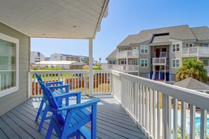 A wooden deck with blue chairs and a white railing overlooking a residential area with houses and a clear sky. - Unwind Poolside, Walk to Shore! Port Aransas Condo (Port Aransas)