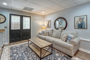 A living room with a sofa, coffee table, patterned rug, wall-mounted clock, and artwork. - Wooded Extended Retreat: 15 Mi to Lake Lanier! (Cumming)