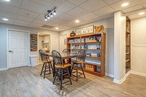 A dining area with a wooden table and chairs, a bookshelf with various items, and a sign that reads 'Welcome to Our Place'. - Wooded Extended Retreat: 15 Mi to Lake Lanier! (Cumming)