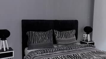 Une chambre moderne avec une couvre-lit à motifs zébrés, une tête de lit noire et deux tables de chevet surmontées de lampes rondes noires.