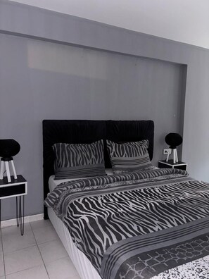 Un dormitorio moderno con una colcha de estampado de cebra, un cabecero negro y dos mesitas de noche con lámparas redondas negras.