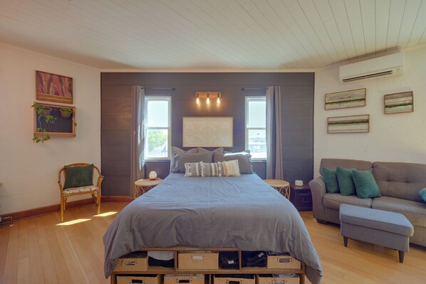 A bedroom with a bed, a nightstand, a chair, a sofa, and a wall with artwork.