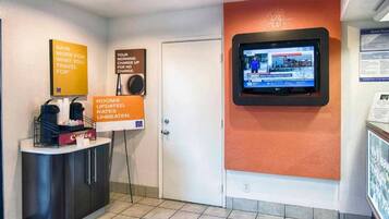Zona de recepción de hotel con pantalla digital mostrando información, mostrador con servicios y carteles indicando tarifas y novedades.