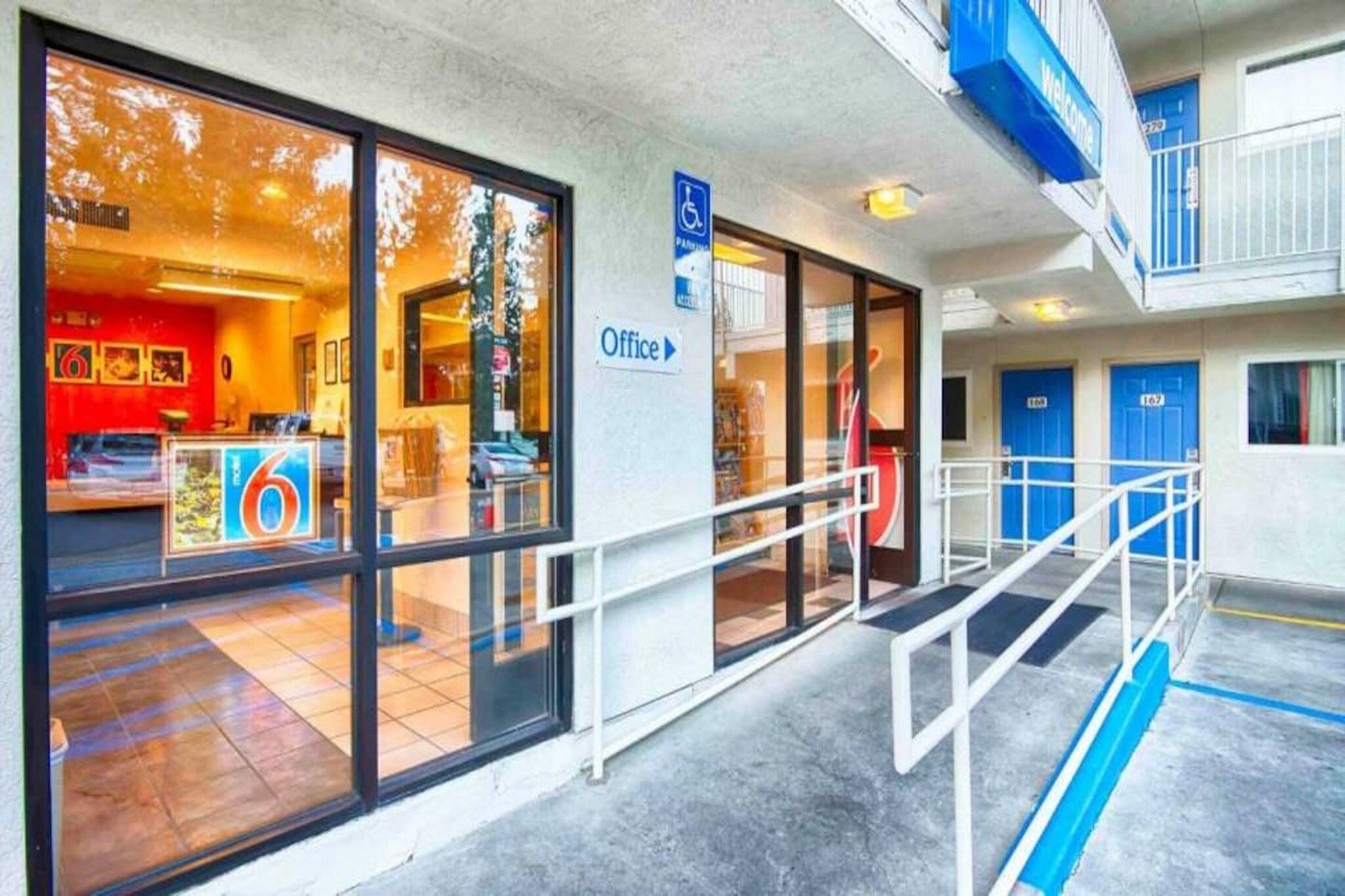 Entrada de hotel com área de recepção, placa de escritório e vaga de estacionamento para deficientes.