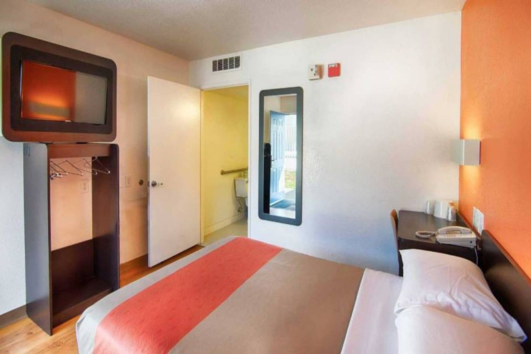 Une chambre d’hôtel comprenant un lit, une télévision, une table de chevet avec un téléphone et une porte donnant accès à une salle de bain.