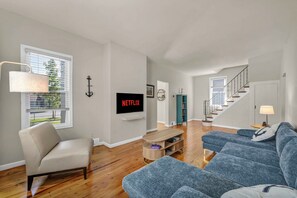 Ein modernes Wohnzimmer mit einer Couch, einem Sessel, einem Fernseher und einer Treppe, die zu einer anderen Ebene führt.