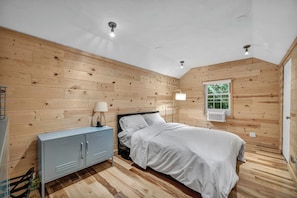 Ein Schlafzimmer mit Holzwand, einem Bett, einem Nachttisch mit Lampe und einem Fenster mit Klimaanlage.