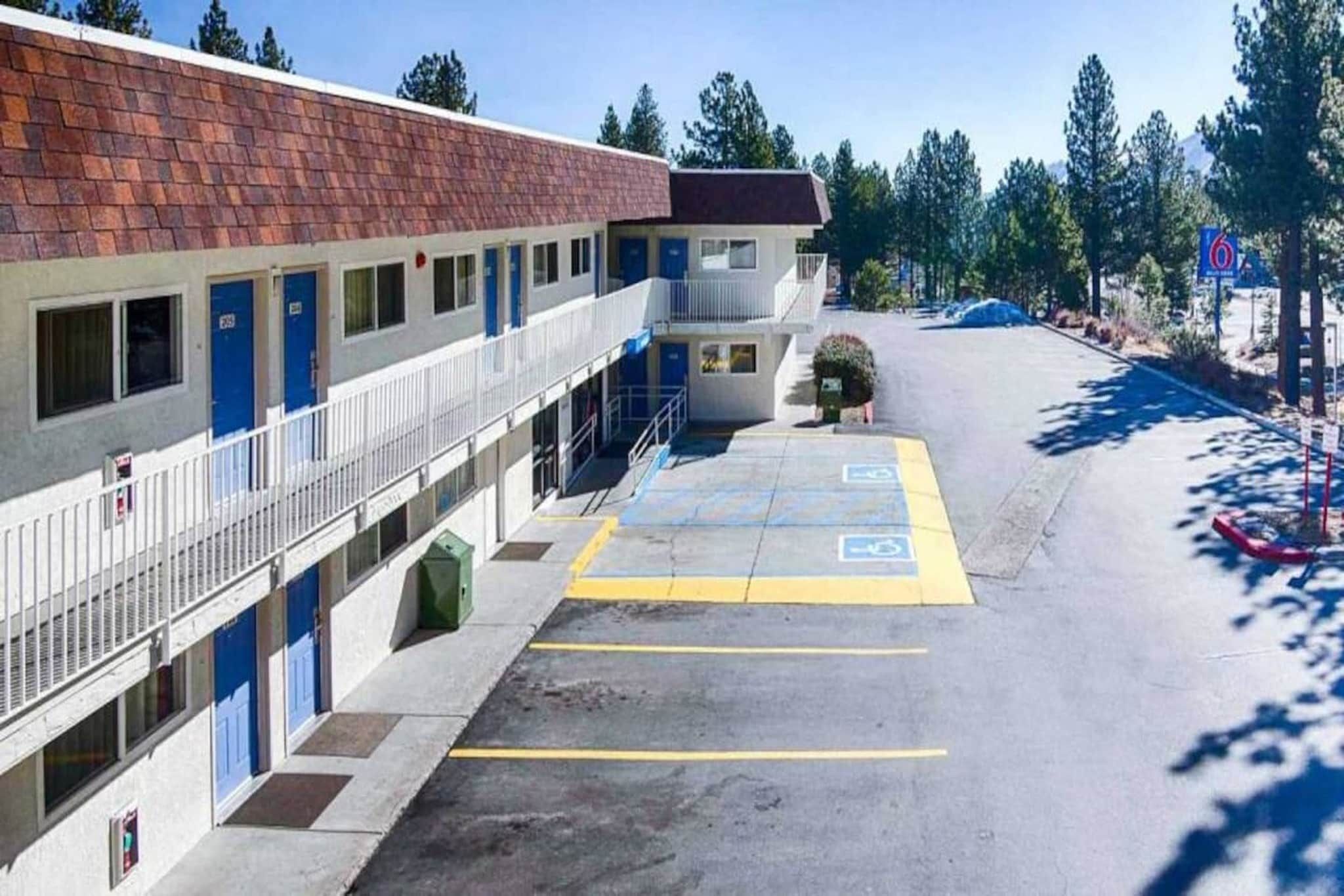 A motel with a parking lot, a small building with a red roof, and a blue sign indicating the number 6.