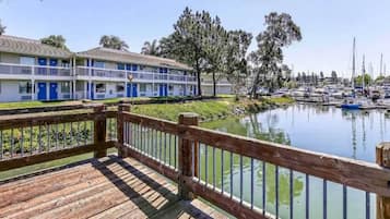 A wooden deck overlooking a marina with boats, a building with blue doors, and trees in the background.